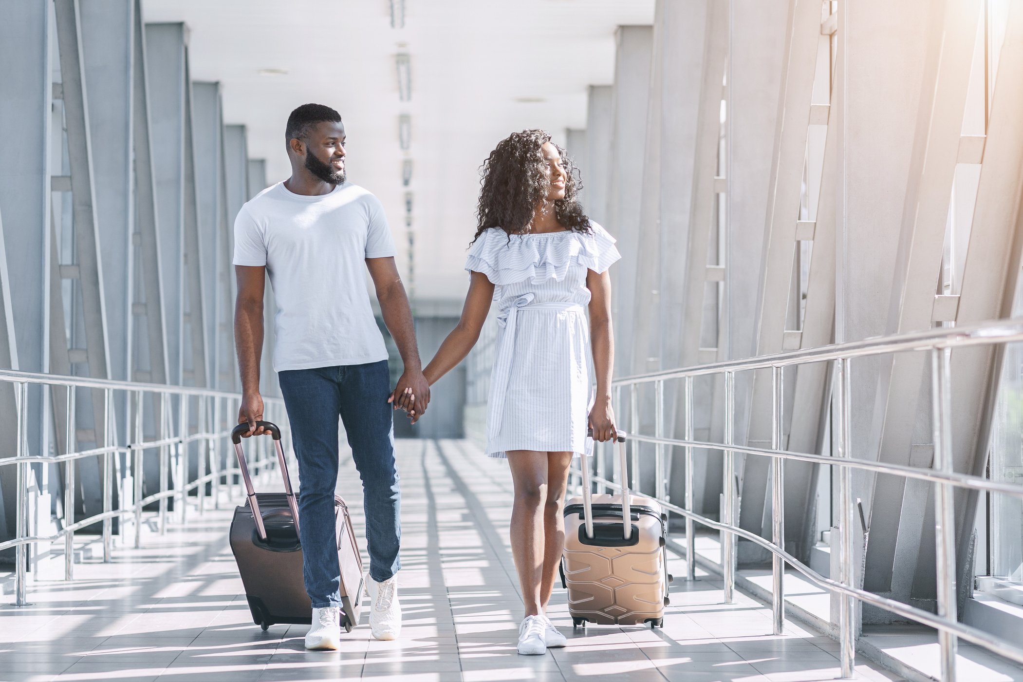 Flight resumption. Happy black couple of travelers walking at airport termina